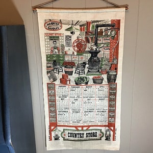 May include: A vintage 1967 calendar tea towel featuring a country store scene with a red, white, and blue color scheme. The towel includes a calendar for each month of the year and the text "Harness Saddles", "U.S. Post Office", and "Country Store".