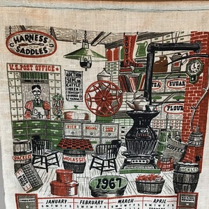 May include: A vintage 1967 calendar tea towel with a red, white, and green color scheme. The towel features a depiction of a general store with various items for sale, including boots, sugar, flour, coffee, and pickles. The text "HARNESS SADDLES" and "U.S. POST OFFICE" are visible at the top of the towel.
