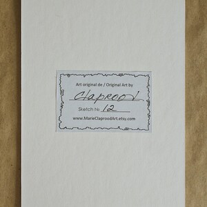 May include: A rectangular white card featuring a central label with a decorative border. The label contains the text: Art original de / Original Art by Claprood, Sketch No 12, and the website address www.MarieClaproodArt.etsy.com printed in black.