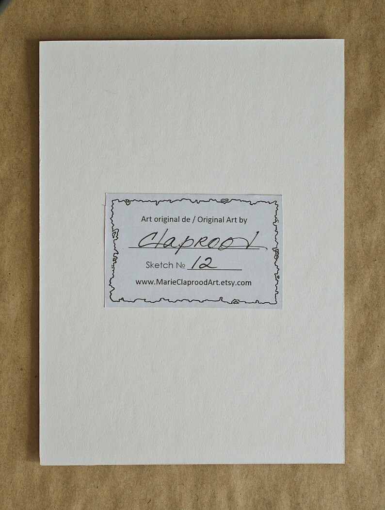 May include: A rectangular white card featuring a central label with a decorative border. The label contains the text: Art original de / Original Art by Claprood, Sketch No 12, and the website address www.MarieClaproodArt.etsy.com printed in black.