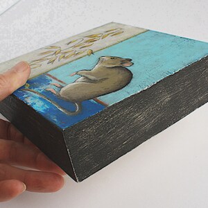 May include: A small wooden box with a painted scene of a brown mouse sitting on a blue and white background. The box is painted black on the edges.
