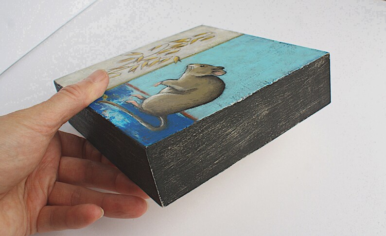 May include: A small wooden box with a painted scene of a brown mouse sitting on a blue and white background. The box is painted black on the edges.