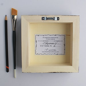 May include: The back of a framed painting with a white mat and a cream-colored backing. The backing has a label with the text "Art original de Original Art by Marie Claprood De la s&eacute;rie dad Variations - No. 6"x 6" Variations - No. 14 www.MarieClaproodArt.etsy.com".