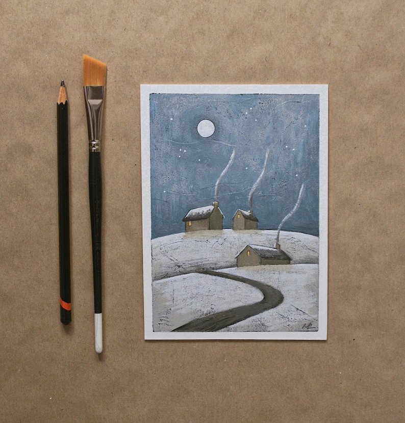 May include: A rectangular painting on paper depicting a snowy landscape with three small houses under a night sky with a full moon and stars. A black pencil and a flat-tipped paintbrush with a black handle are positioned to the left of the art.