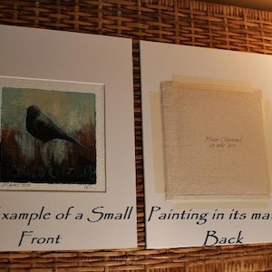 May include: Two white mat boards displaying a small square painting. The left board shows the front of a painting featuring a black bird against a textured background. The right board shows the back of the painting with text reading Marie Chapuis 25 ao&ucirc;t 2015.