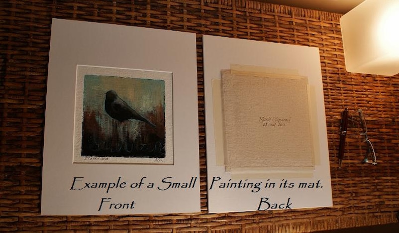 May include: Two white mat boards displaying a small square painting. The left board shows the front of a painting featuring a black bird against a textured background. The right board shows the back of the painting with text reading Marie Chapuis 25 ao&ucirc;t 2015.