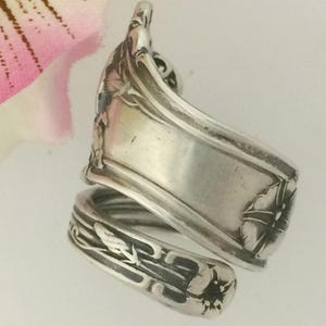 May include: Silver spoon ring with a floral design. The ring is made from a vintage spoon and features a delicate floral pattern with a twisted band.