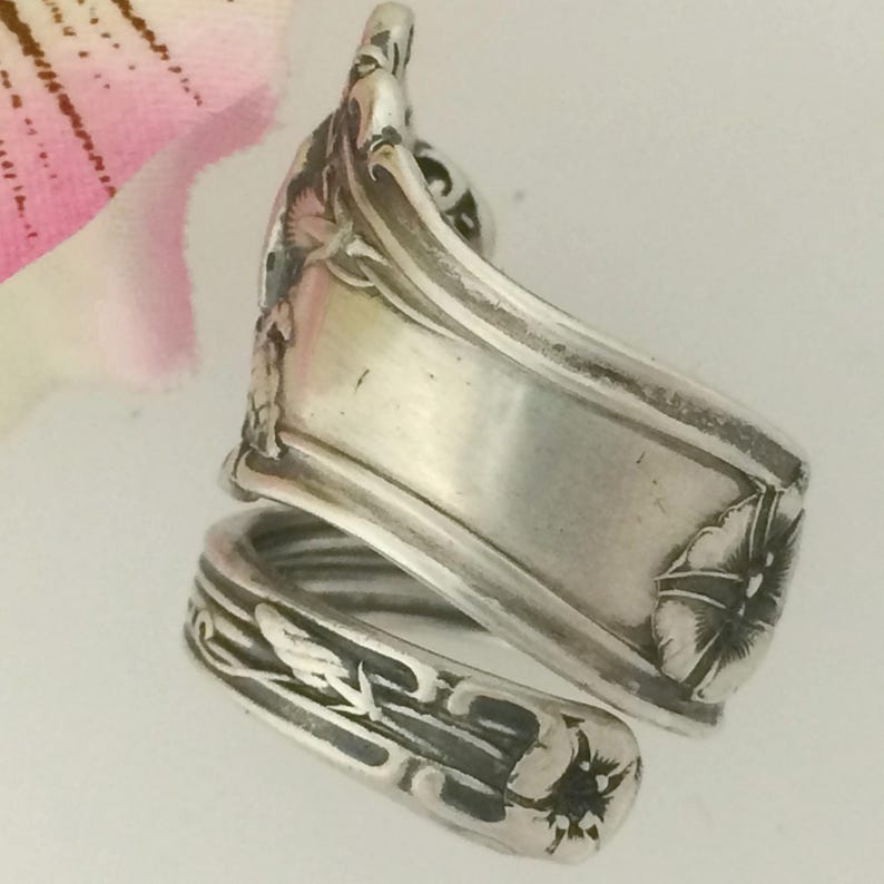 May include: Silver spoon ring with a floral design. The ring is made from a vintage spoon and features a delicate floral pattern with a twisted band.