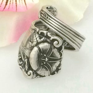 May include: A silver ring made from a vintage spoon, featuring a detailed floral design with a single flower in the center.