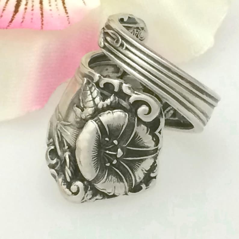May include: A silver ring made from a vintage spoon, featuring a detailed floral design with a single flower in the center.