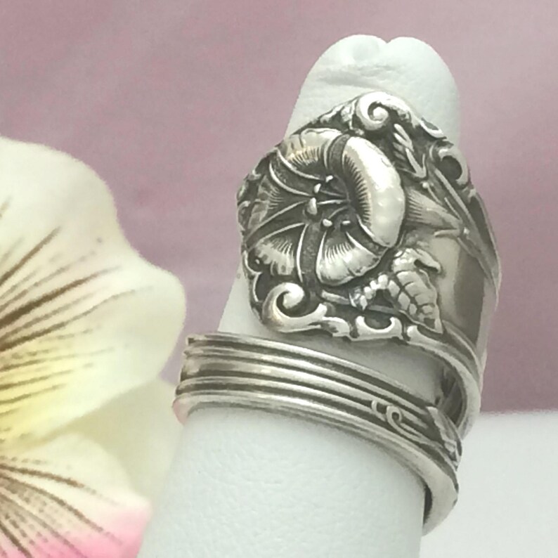 May include: A silver ring made from a vintage spoon with a detailed floral design. The ring is adjustable and features a delicate flower with leaves.