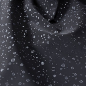 Könnte beinhalten: Nahaufnahme eines dunkelgrauen Stoffes mit wasserabweisender Beschichtung. Der Stoff ist mit kleinen, runden Wassertropfen bedeckt.