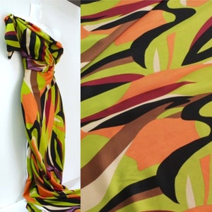 Pode incluir: Um vestido de um ombro só com uma estampa abstrata colorida em tons de verde, laranja, marrom, preto e roxo.