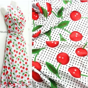 May include: White fabric with a repeating pattern of red cherries with green stems and leaves on a white background with small black polka dots.