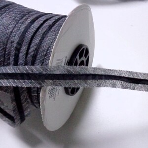 May include: A spool of black and gray striped ribbon with a black edge. The ribbon is wound around a white cardboard spool.