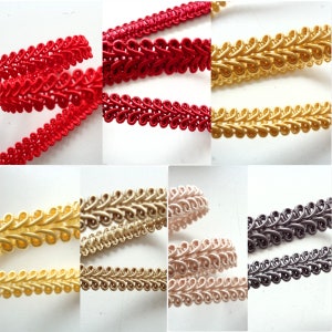 Op de afbeelding: Assortiment van decoratieve trim in verschillende kleuren, waaronder rood, goud en grijs. De trim is gemaakt van een geweven stof met een gelust ontwerp.