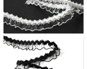 May include: Two spools of ruffled trim, one white and one black. The trim is made of a sheer fabric with small, round beads along the edge.