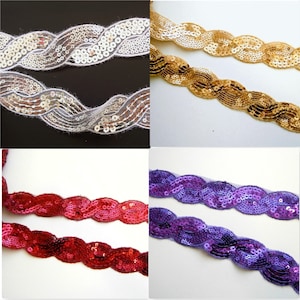 Puede incluir: Cuatro carretes de ribete de lentejuelas en blanco, dorado, rojo y morado. El ribete está hecho de una tela tejida con lentejuelas cosidas en un patrón ondulado.