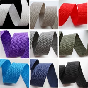 Könnte beinhalten: Eine Sammlung von 10 verschiedenen Farben von Gurtbändern. Die Bänder sind alle 5 cm breit und aus strapazierfähigem Nylon gefertigt. Die Farben umfassen Weiß, Grau, Rot, Lila, Blau, Türkis, Marineblau, Schwarz und Grün.