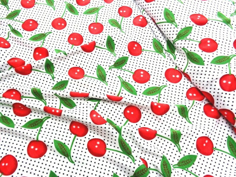 May include: White fabric with a repeating pattern of red cherries with green stems and leaves on a white background with small black polka dots.