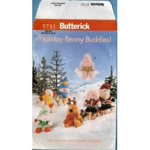 May include: A vintage Butterick pattern envelope, featuring the text "Holiday Beany Buddies!" and the number 5731. The illustration shows several small, plush holiday-themed figures, including a snowman, a reindeer, and a Santa Claus on a sled, set against a snowy mountain backdrop.