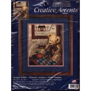 May include: Cross stitch pattern featuring a teddy bear sitting on a quilt with a house and apple in the background. The pattern is titled "Home Sweet Home" and is from Creative Accents.