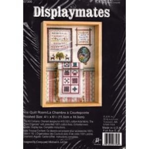May include: A framed cross-stitch kit labeled "Displaymates." The kit includes a miniature quilt room scene with various cross-stitched designs, including a quilt, framed text, and decorative elements. The finished size is 4.5 x 6.5 inches.