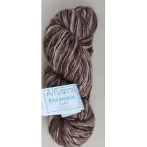 May include: A skein of Artyarns Ensemble Light yarn in shades of brown and white. The yarn is tightly wound and has a soft, textured appearance. A white label with blue text reads "Artyarns Ensemble Light".