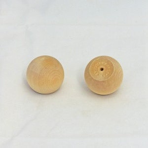 May include: Two wooden balls, one with a small hole in the center. The balls are smooth and light brown in color.