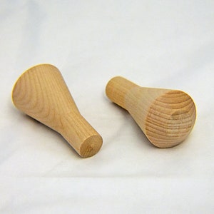 May include: Two unfinished wooden furniture legs with a light brown color. Each leg has a rounded top and a narrower, cylindrical base. The legs are designed for furniture construction or repair.
