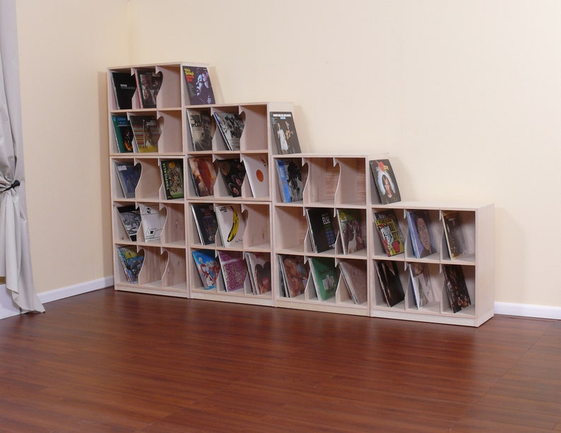 May include: A set of five wooden record shelves with a staggered design. The shelves are filled with vinyl records. The shelves are made of light wood and have a natural finish.