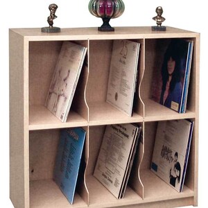 May include: A light wood record storage cabinet with six compartments. Each compartment has a divider to hold vinyl records upright. The cabinet has a shelf on top for displaying decorative items.