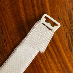 May include: White hook and loop fastener with a white plastic slider. The hook and loop fastener is attached to a white plastic slider.