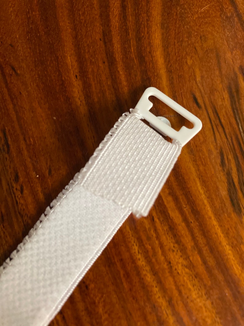 May include: White hook and loop fastener with a white plastic slider. The hook and loop fastener is attached to a white plastic slider.