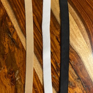 May include: Three elastic bands in different colors: beige, white, and black. The bands are lying flat on a wooden surface.