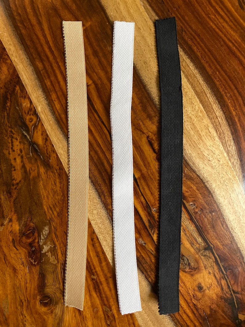 May include: Three elastic bands in different colors: beige, white, and black. The bands are lying flat on a wooden surface.