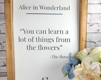May include: A framed print with a white background and black text. The text reads "Alice in Wonderland" and a quote from the book: "You can learn a lot of things from the flowers" -The flowers. The number 43 is printed in black at the bottom of the print.