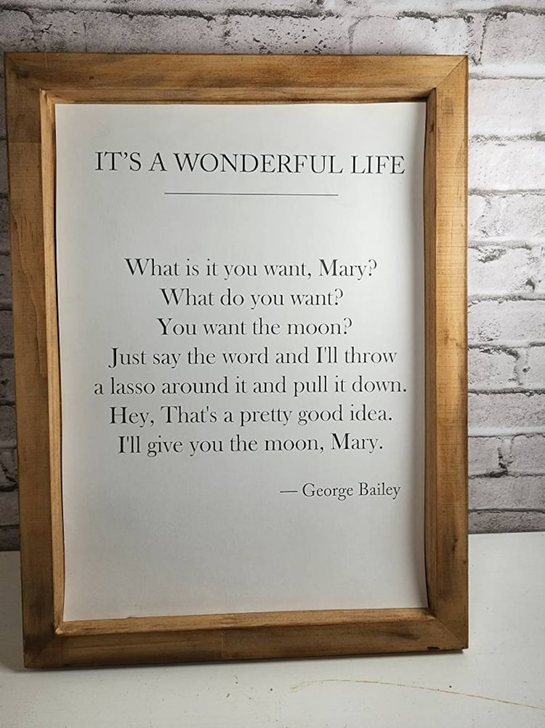 May include: A framed print with a white background and black text. The text reads "IT'S A WONDERFUL LIFE" and includes a quote from the movie: "What is it you want, Mary? What do you want? You want the moon? Just say the word and I'll throw a lasso around it and pull it down. Hey, That's a pretty good idea. I'll give you the moon, Mary. - George Bailey"