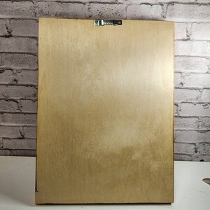 May include: A plain, light brown wooden frame with a metal hanging hook on the back.