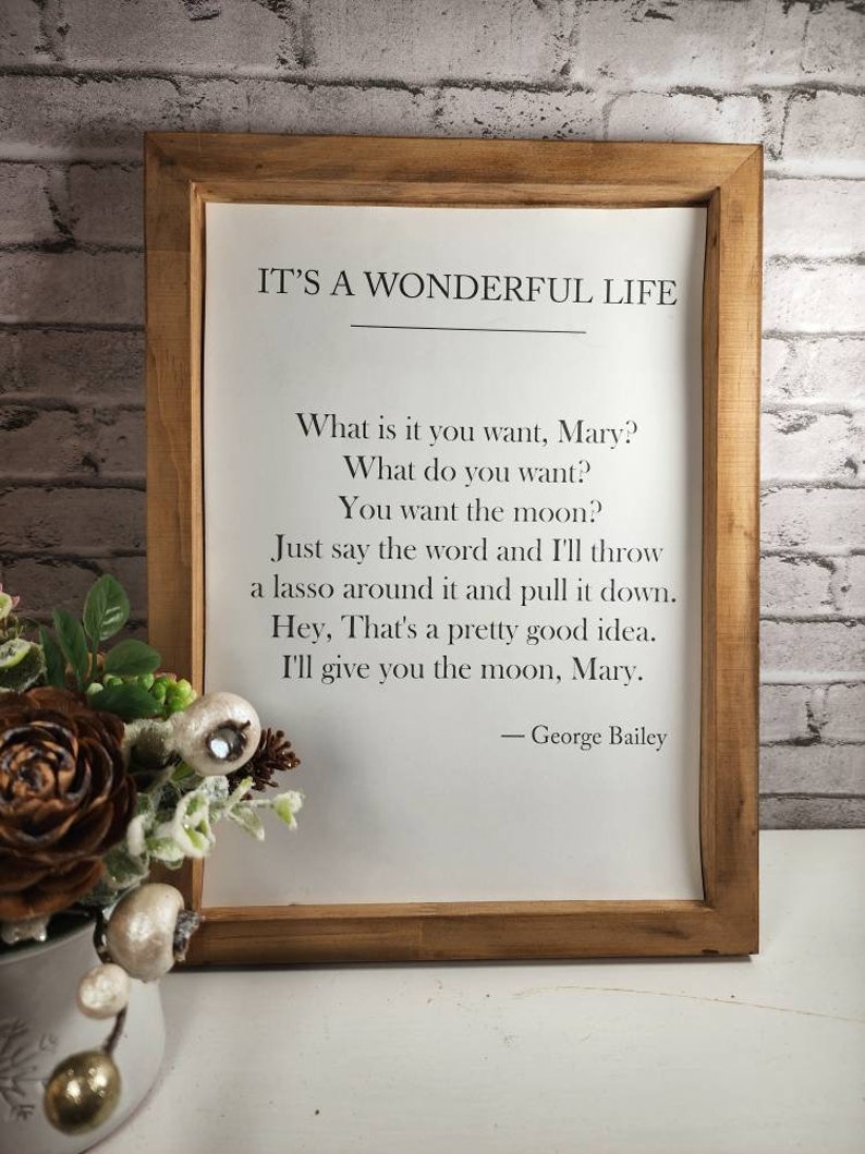 May include: A framed print with a white background and black text. The text reads "IT'S A WONDERFUL LIFE" and includes a quote from the movie. The quote reads: "What is it you want, Mary? What do you want? You want the moon? Just say the word and I'll throw a lasso around it and pull it down. Hey, That's a pretty good idea. I'll give you the moon, Mary." The quote is attributed to "George Bailey".