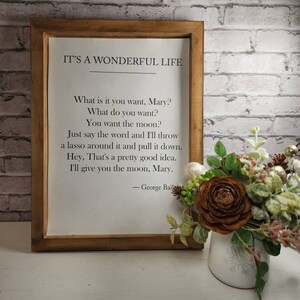 May include: A framed print with a white background and black text. The text reads "IT'S A WONDERFUL LIFE" and includes a quote from the movie. The quote reads "What is it you want, Mary? What do you want? You want the moon? Just say the word and I'll throw a lasso around it and pull it down. Hey, That's a pretty good idea. I'll give you the moon, Mary." The quote is attributed to "George Bailey".
