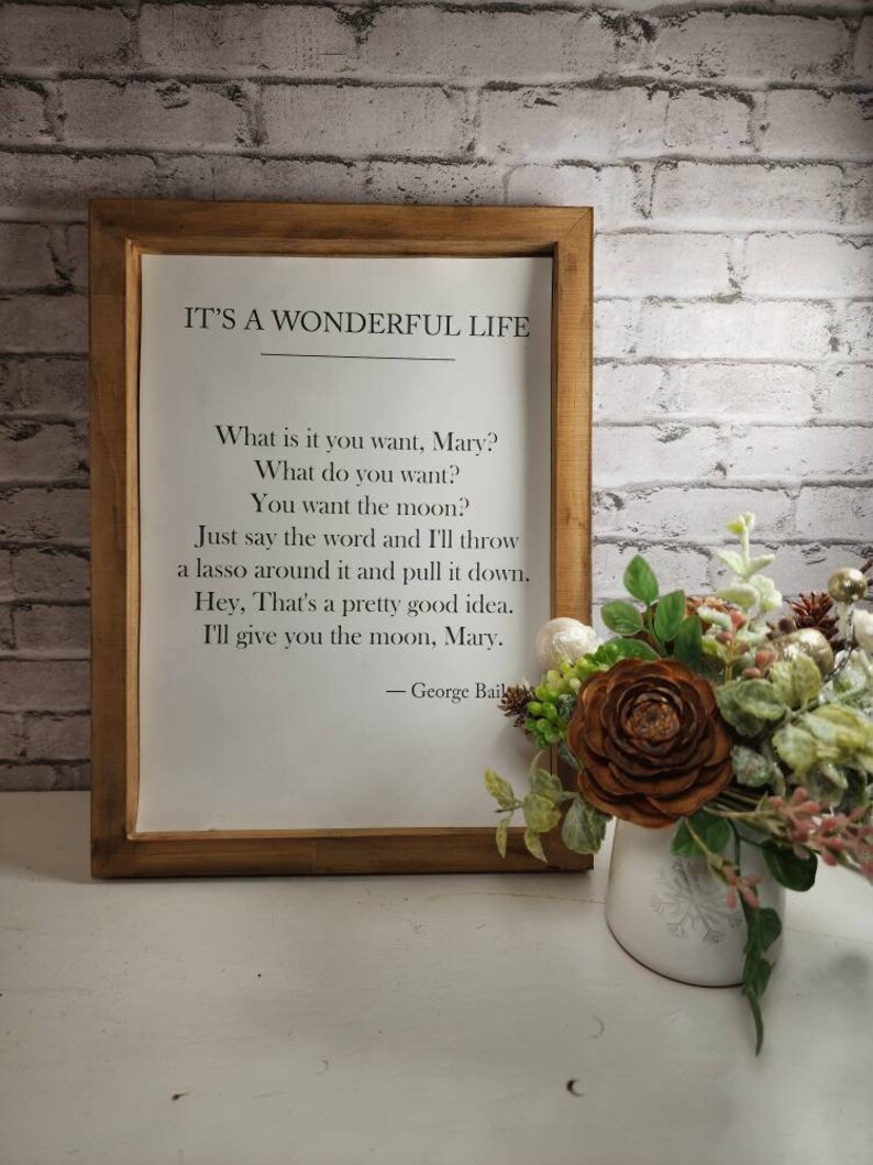 May include: A framed print with a white background and black text. The text reads "IT'S A WONDERFUL LIFE" and includes a quote from the movie. The quote reads "What is it you want, Mary? What do you want? You want the moon? Just say the word and I'll throw a lasso around it and pull it down. Hey, That's a pretty good idea. I'll give you the moon, Mary." The quote is attributed to "George Bailey".