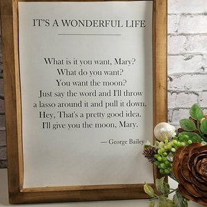 May include: A framed print with a white background and black text. The text reads "It's a Wonderful Life" and includes a quote from the movie: "What is it you want, Mary? What do you want? You want the moon? Just say the word and I'll throw a lasso around it and pull it down. Hey, That's a pretty good idea. I'll give you the moon, Mary. - George Bailey"