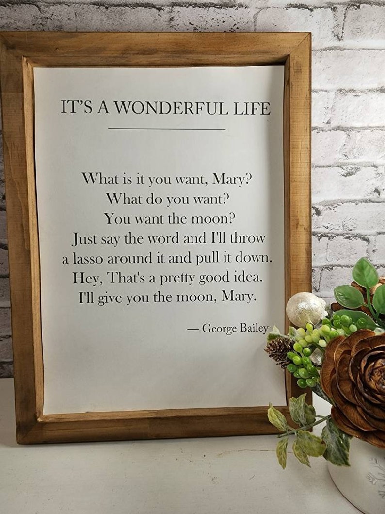 May include: A framed print with a white background and black text. The text reads "It's a Wonderful Life" and includes a quote from the movie: "What is it you want, Mary? What do you want? You want the moon? Just say the word and I'll throw a lasso around it and pull it down. Hey, That's a pretty good idea. I'll give you the moon, Mary. - George Bailey"