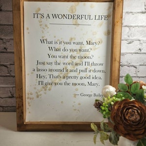 May include: A framed print with a white background and brown splatter paint. The print features a quote from the movie "It's a Wonderful Life" by George Bailey. The quote reads: "What is it you want, Mary? What do you want? You want the moon? Just say the word and I'll throw a lasso around it and pull it down. Hey, That's a pretty good idea. I'll give you the moon, Mary."
