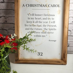 May include: A framed print with a white background and black text. The text is a quote from "A Christmas Carol" by Charles Dickens. The quote reads: "I will honor Christmas in my heart, and try to keep it all the year. I will live in the Past, the Present, and the Future. The Spirits of all Three shall strive within me." - Scrooge. The number 32 is printed at the bottom of the print.