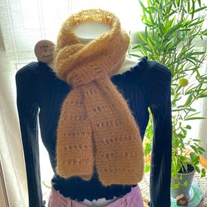May include: A brown fuzzy knit scarf with a lacy pattern. The scarf is draped around a mannequin wearing a black sweater.