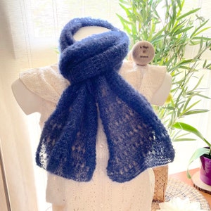 May include: A blue knitted scarf with a lacy pattern. The scarf is draped over a white shirt on a mannequin.