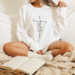 May include: A white long-sleeved shirt with the word "faith" written vertically in a stylized cross shape.