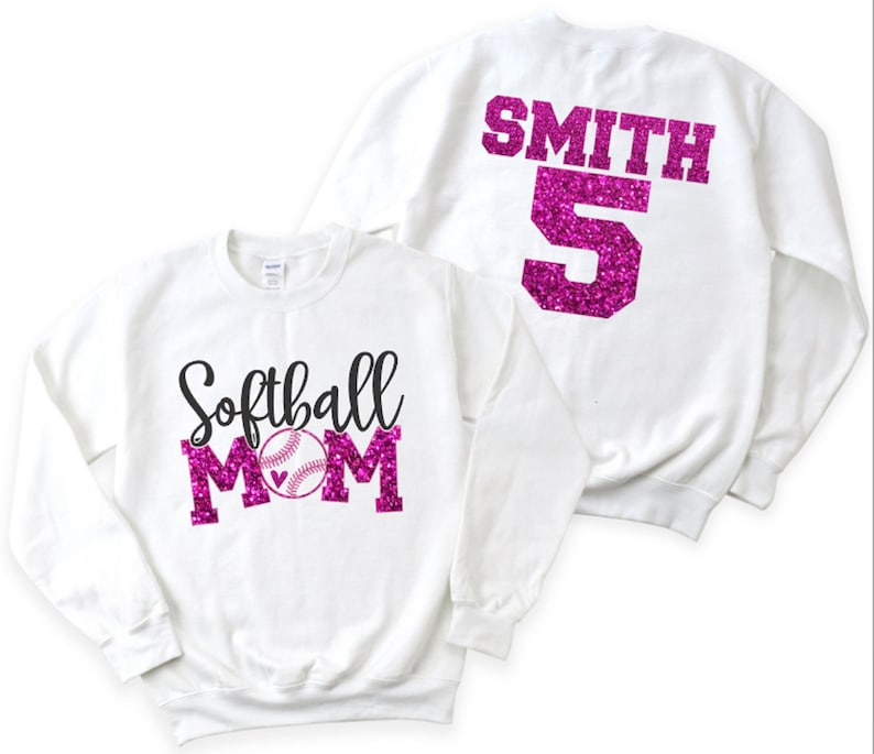 May include: White sweatshirt with pink glitter text that says "Softball Mom" with a baseball graphic. The back of the sweatshirt has pink glitter text that says "SMITH 5".